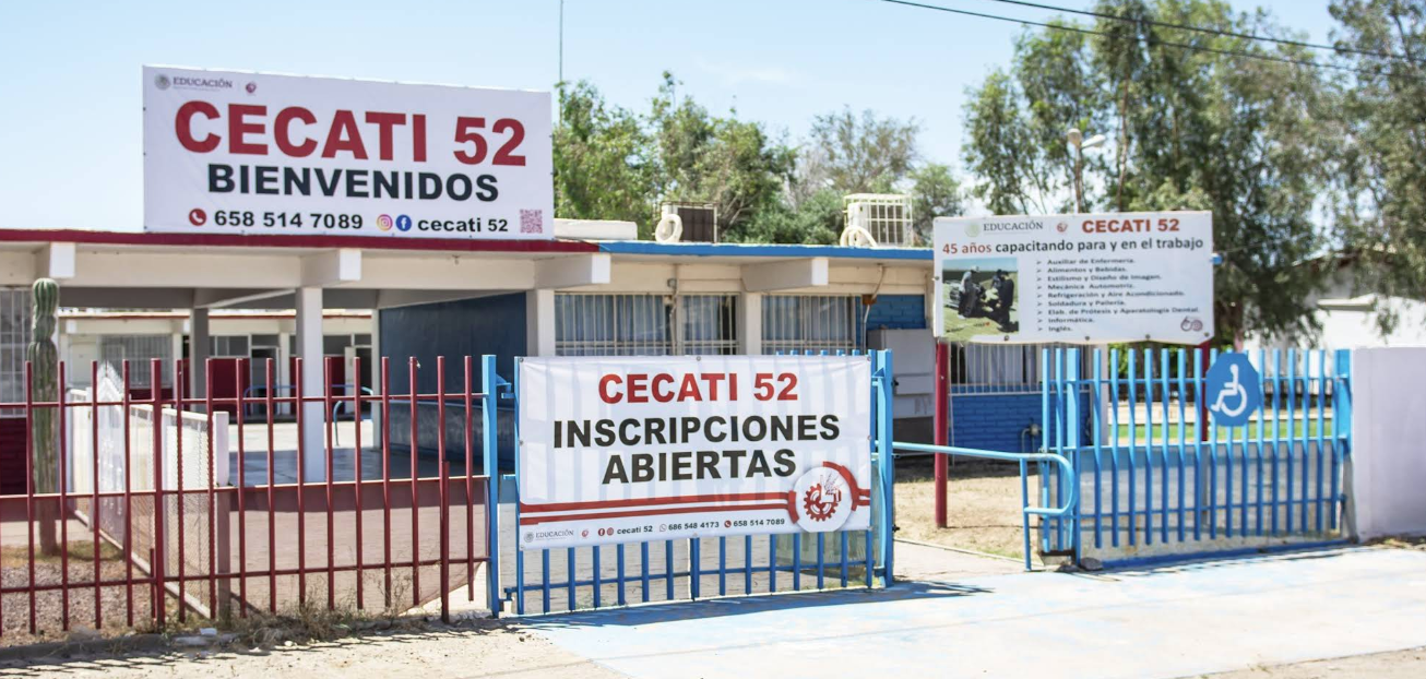 En la fotografía se muestra la entrada del plantel conformada por una reja color azul. A la mitad de la reja hay un espacio que permite el acceso a las instalaciones mediante una rampa de acceso. En la fachada hay tres carteles: en uno de ellos se puede leer el contacto y en letras grandes CECATI 52 BIENVENIDOS.
